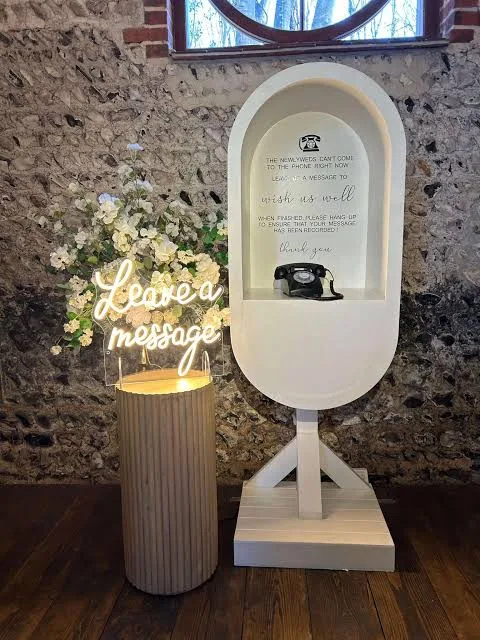 Audio guest book phone booth with a wish us well greeting sign at a wedding venue